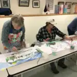 Photo of two people hand painting scenes on a paper scroll crankie