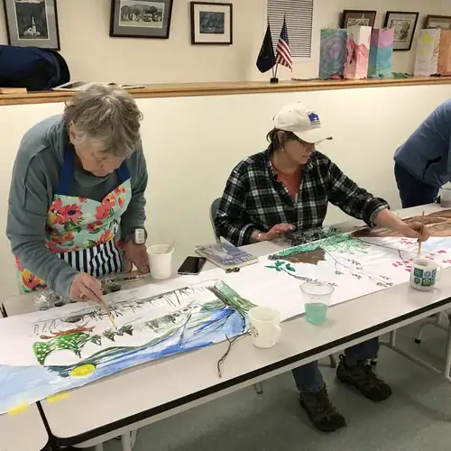 Photo of two people hand painting scenes on a paper scroll crankie