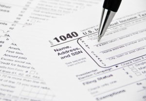 A close-up of a pen resting on a U.S. IRS Form 1040 income tax document, with text fields and instructions visible in the background.