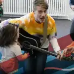 photo of Mr. Aaron playing guitar for young children and parents
