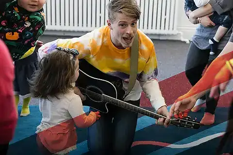 Photo of Mr. Aaron playing guitar for a group of young children and parents