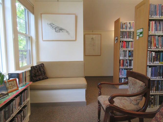 Photo of a corner of the interior of the library with bookshelves plus two large framed drawings hanging on the walls