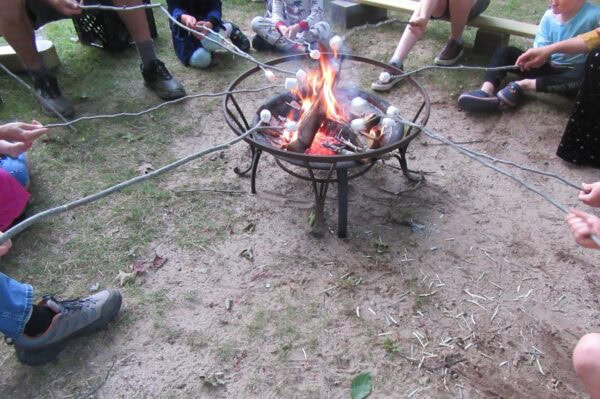 Photo of campfire surrounded by people toasting marshmallows on sticks