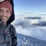 Photo of Michael Whittemore in a parka with a high summit background