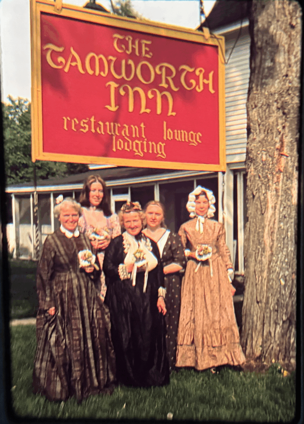 Photo from 1976 of a group of people wearing 18th-century dresses standing in front of the sign for The Tamworth Inn.